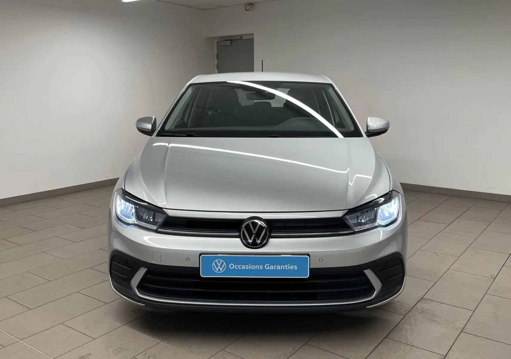 Volkswagen Polo 1.0 TSI 95 BVM5 Life en reflet d'argent vue de face avec phares allumés dans un showroom.