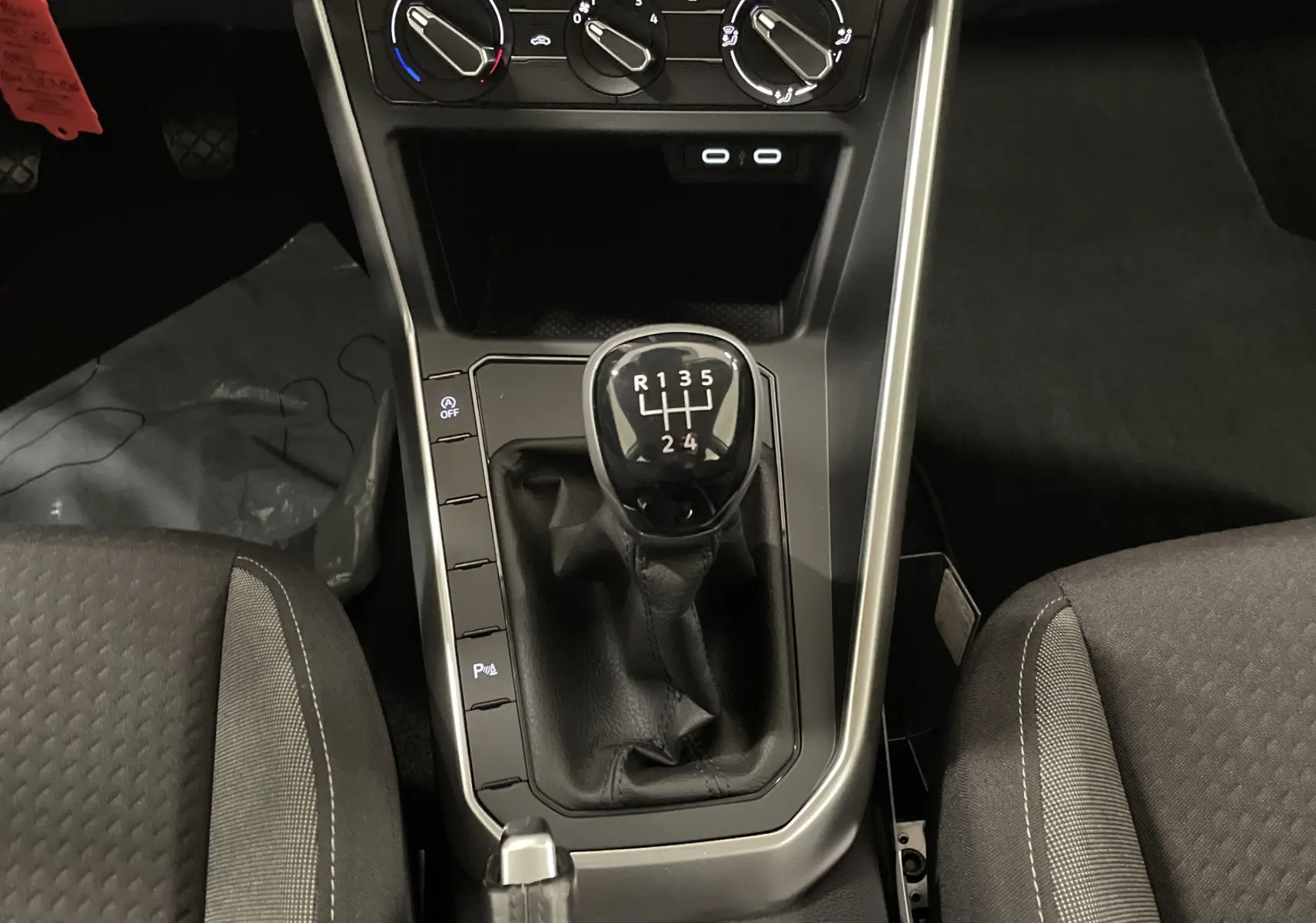 Le levier de vitesses manuel noir au centre de la console d'une Volkswagen Polo 2023 avec sièges gris.