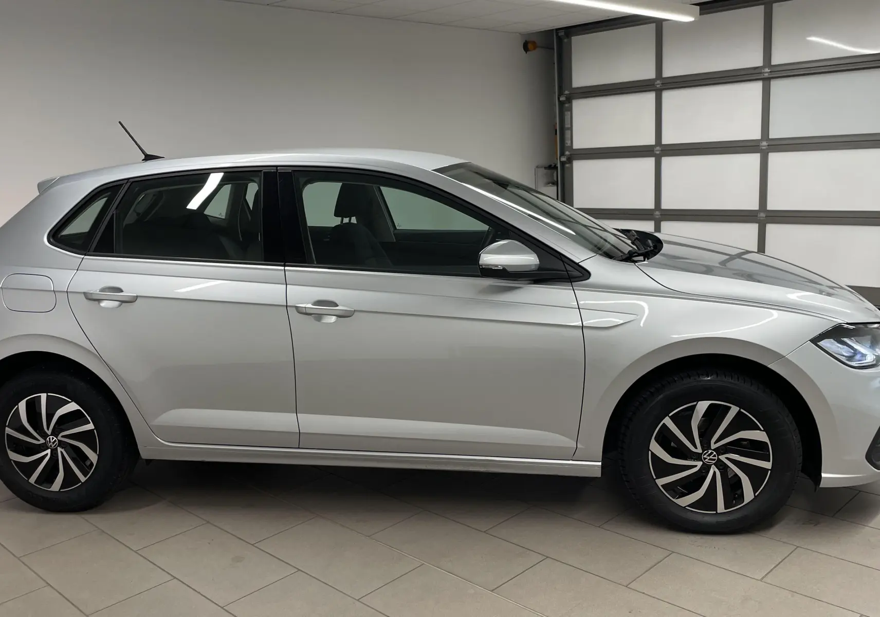 Profil côté gauche d'une Volkswagen Polo 1.0 TSI 95 BVM5 Life en peinture métallisée reflet d'argent, roues alliage noires et argent.