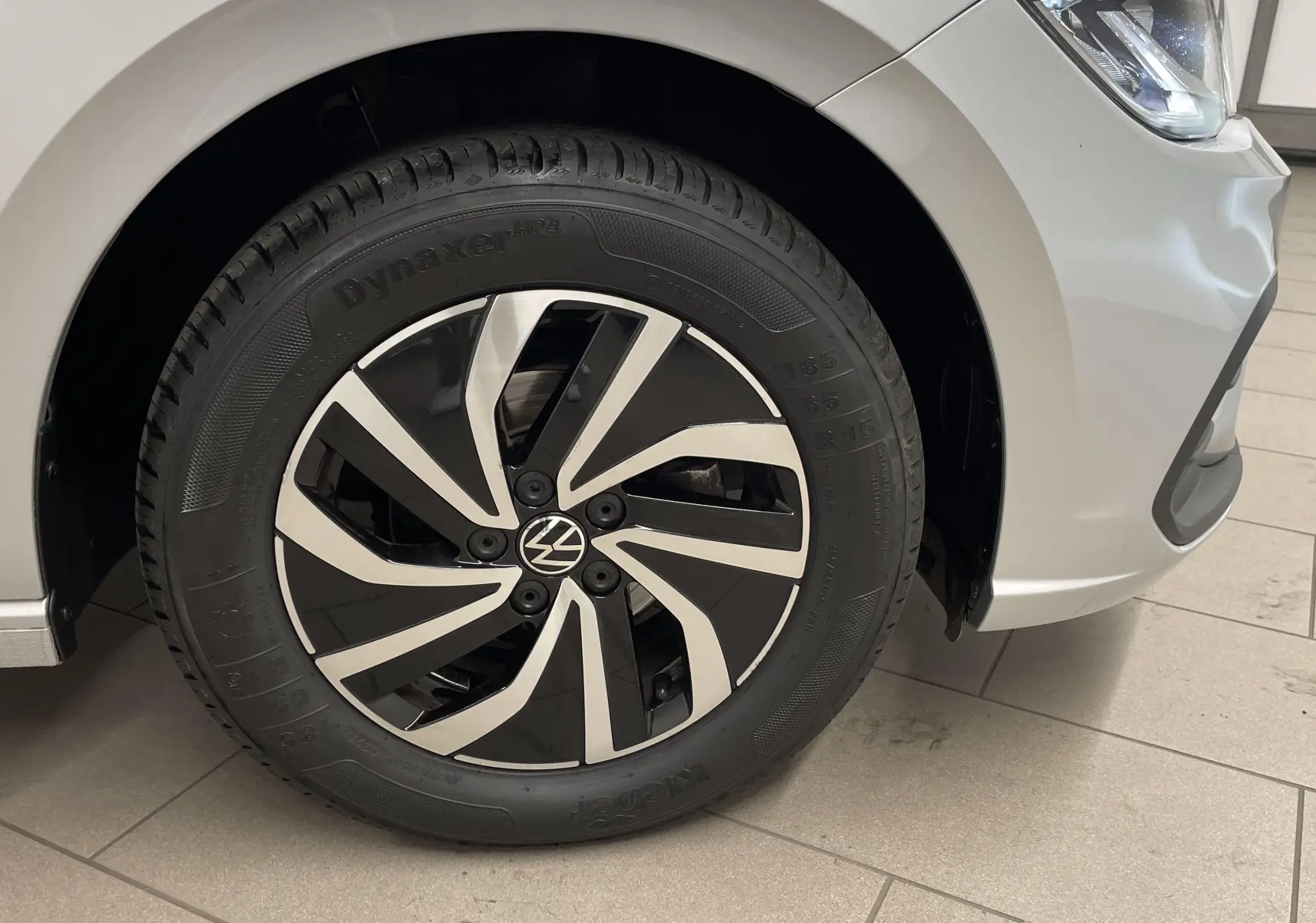 Gros plan sur la roue avant droite d'une Volkswagen Polo 2023 couleur reflet d'argent avec jante noire et argentée.