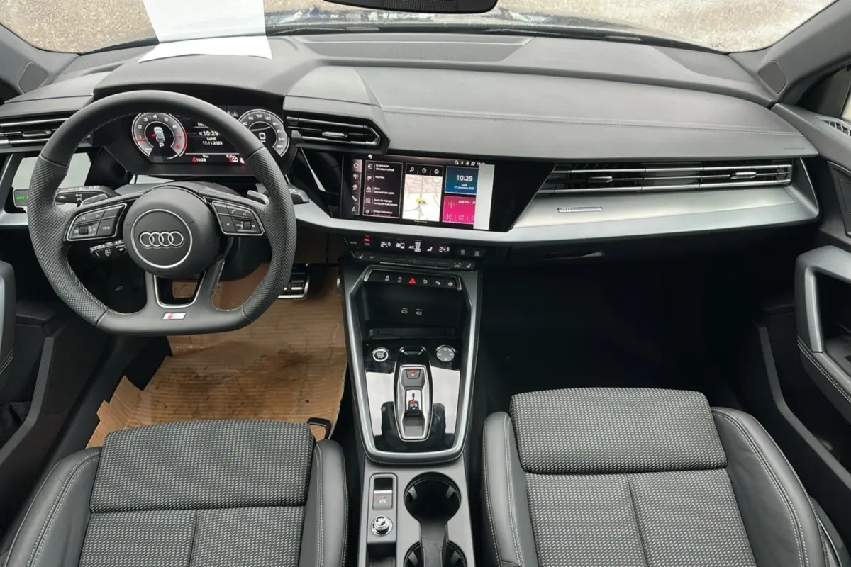 Intérieur Audi A3 2025 vu de face, volant cuir méplat, écran tactile central et sièges sport tissu cuir gris.