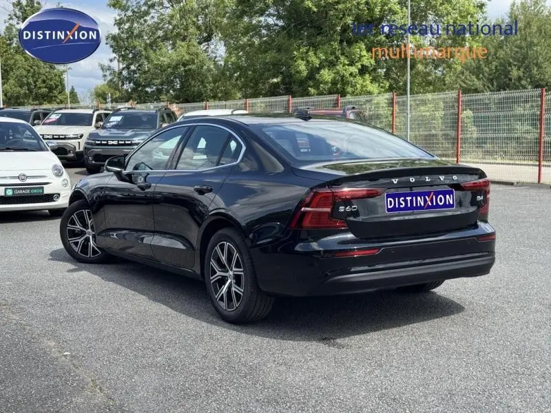 Vue 3/4 arrière droite d'une Volvo S60 2024 noire métallisée avec jantes alu et feux arrière LED distinctifs.