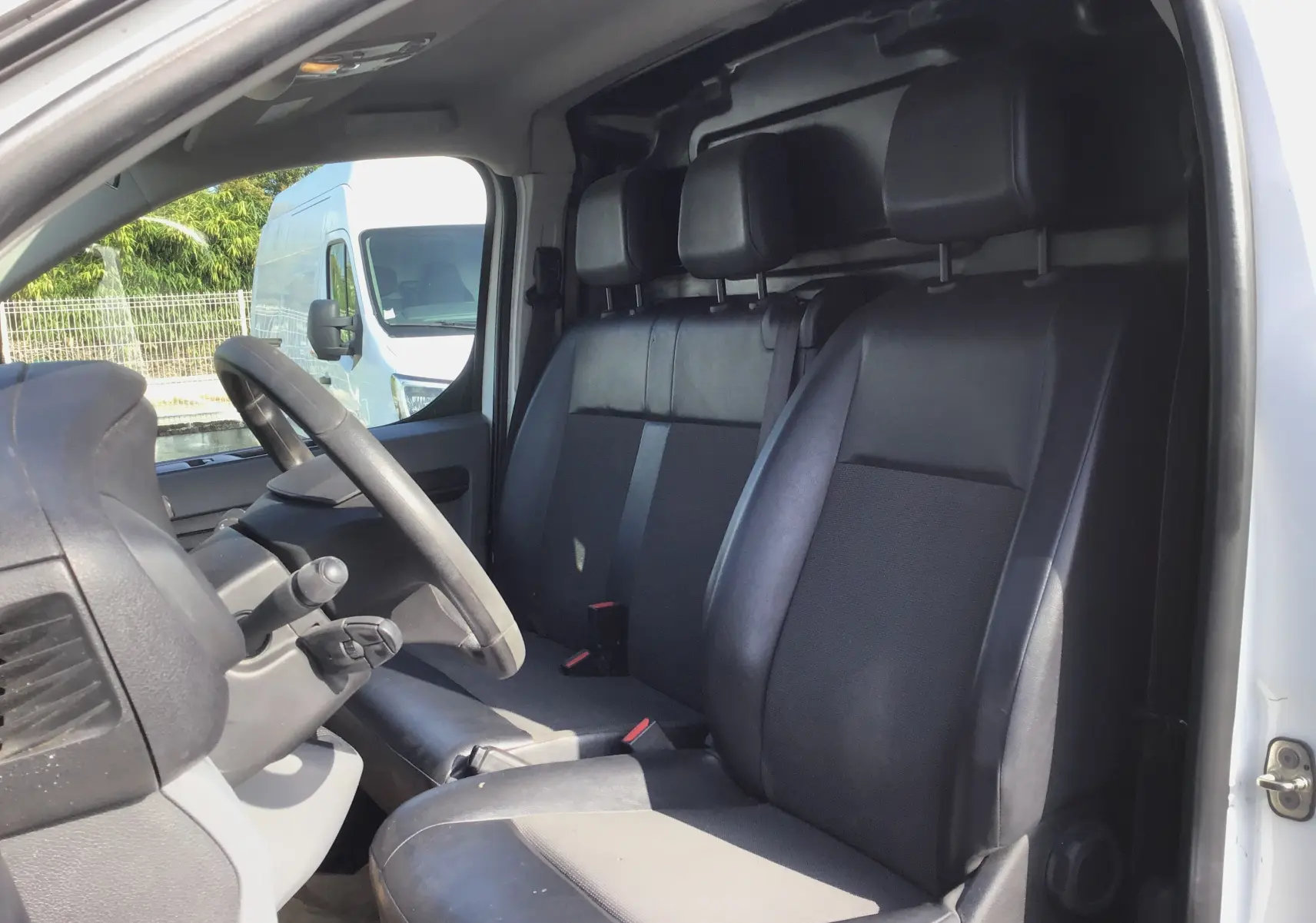 Vue intérieure côté conducteur du Citroën Jumpy blanc 2021, montrant les sièges noirs et le volant.