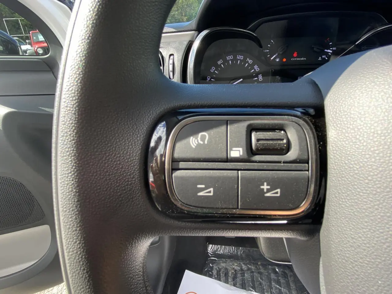 Gros plan sur les commandes audio au volant noir d'une Citroën C3 blanche, tableau de bord et compteur visibles en arrière-plan.