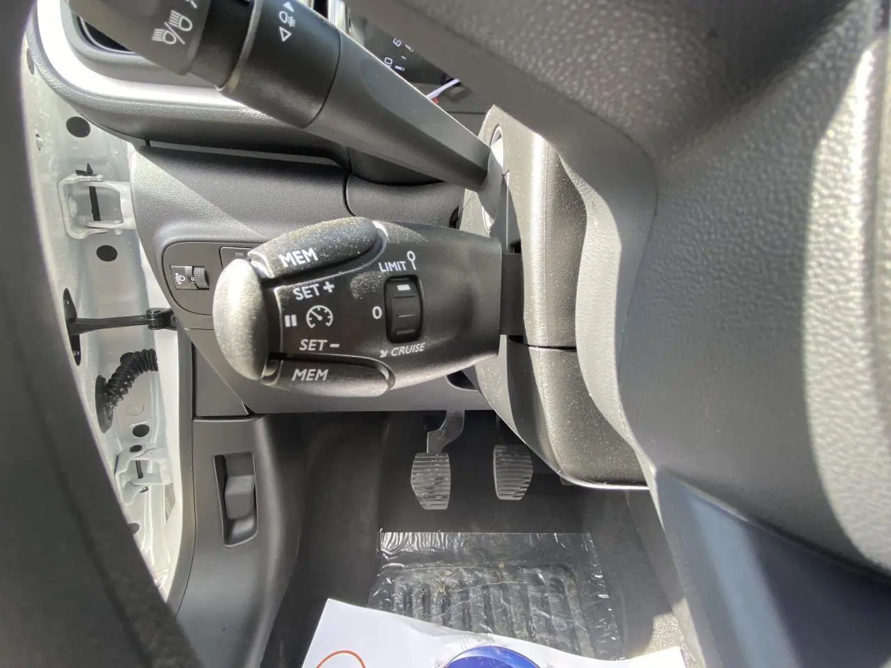 Vue rapprochée sous le volant de la Citroën C3 blanche 2022, montrant les commandes du régulateur de vitesse et les pédales.