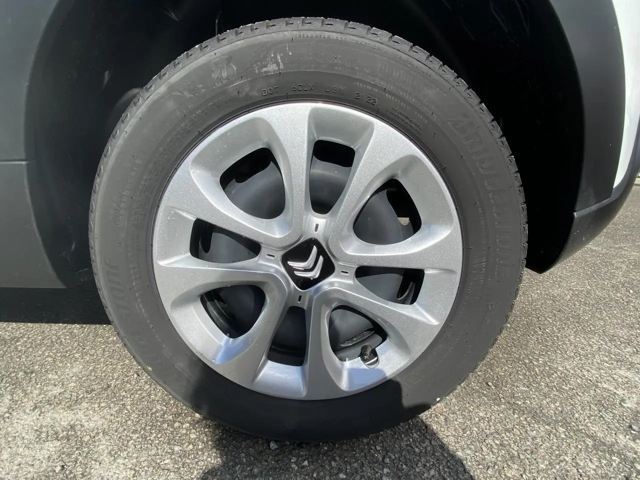 Gros plan sur la roue avant droite de la Citroën C3 blanche 2022 avec enjoliveur argenté à cinq branches arrondies.