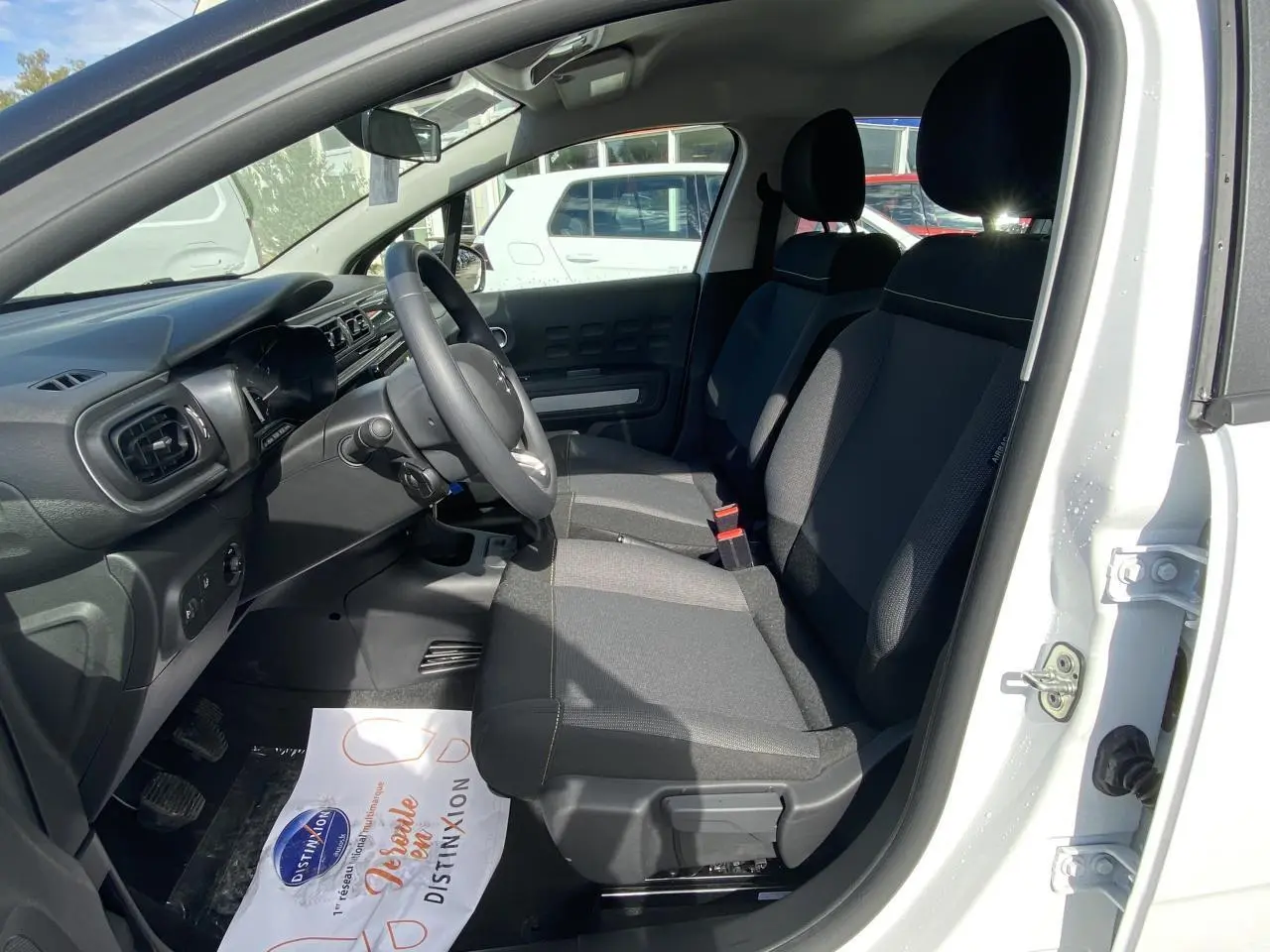 Intérieur avant de la Citroën C3 blanche 2022, montrant les sièges tissu gris et le tableau de bord côté conducteur.