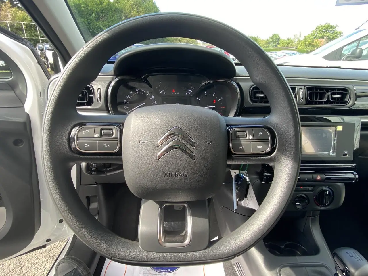 Vue depuis le siège conducteur du tableau de bord et du volant noir d'une Citroën C3 blanche de 2022, avec commandes intégrées.