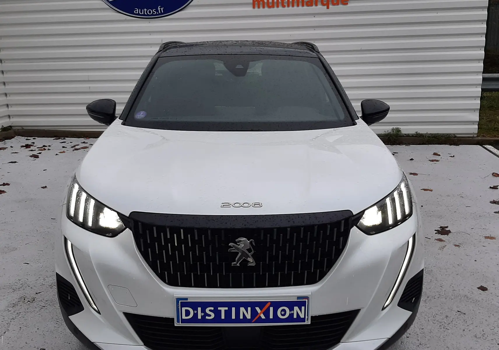 Vue avant d'un Peugeot 2008 blanc nacré avec toit noir, phares allumés et calandre noire distinctive.