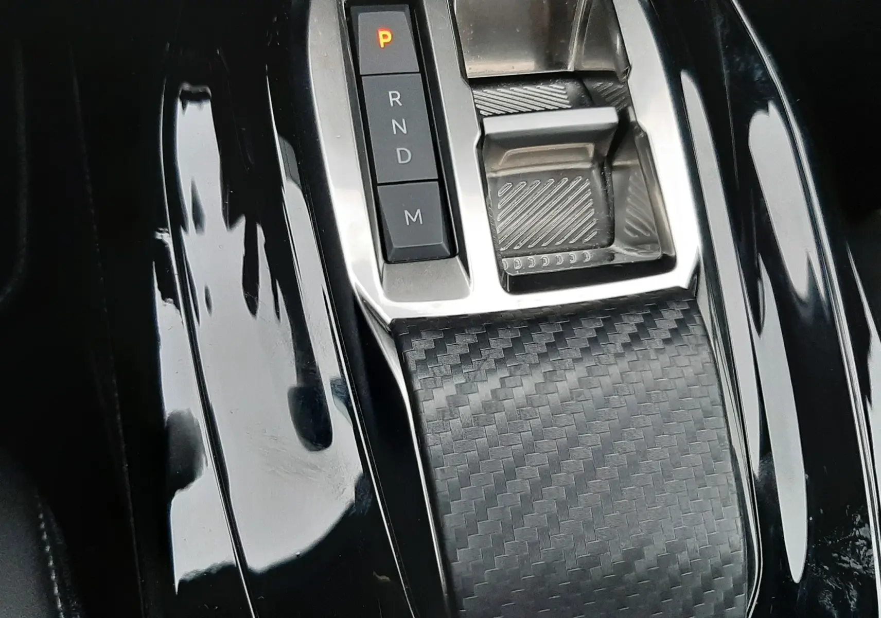Gros plan sur la console centrale noire brillante du Peugeot 2008 2023, avec levier de vitesses automatique et finition carbone.