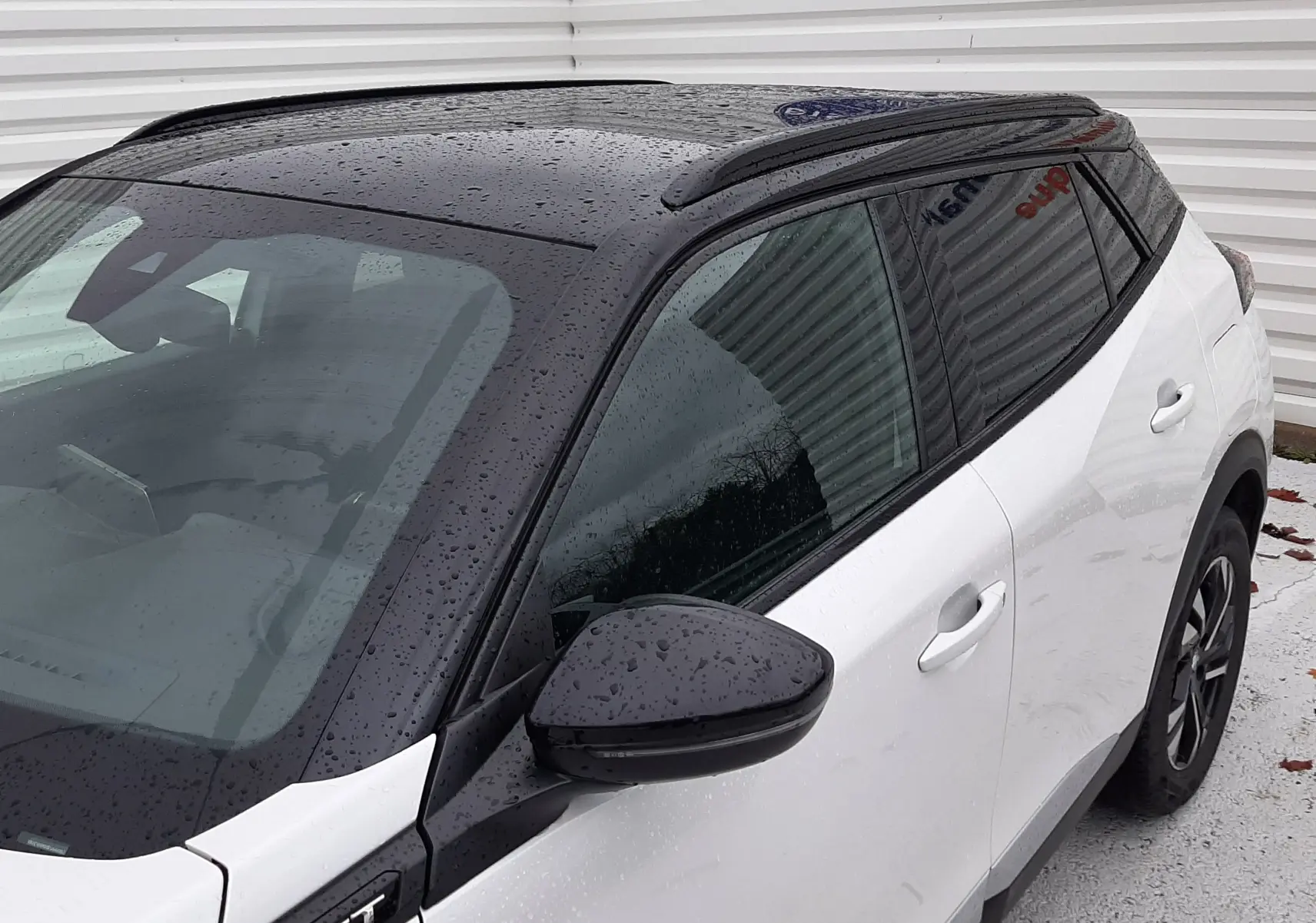 Vue 3/4 avant droit d'un Peugeot 2008 blanc nacré avec toit noir brillant et badge GT sous la pluie.