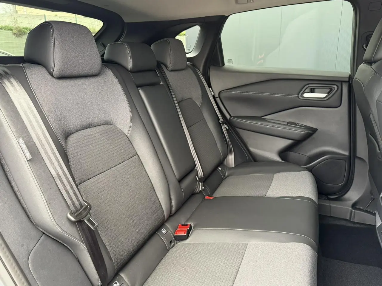 Vue intérieure côté droit des sièges arrière gris et noirs du Nissan Qashqai III e-Power 2025 avec ceintures et appuie-têtes visibles.
