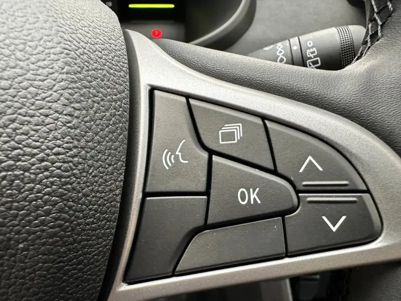 Gros plan sur les commandes multifonctions noires au volant du Dacia Jogger 1.6 hybrid 2025, avec boutons de navigation et validation.