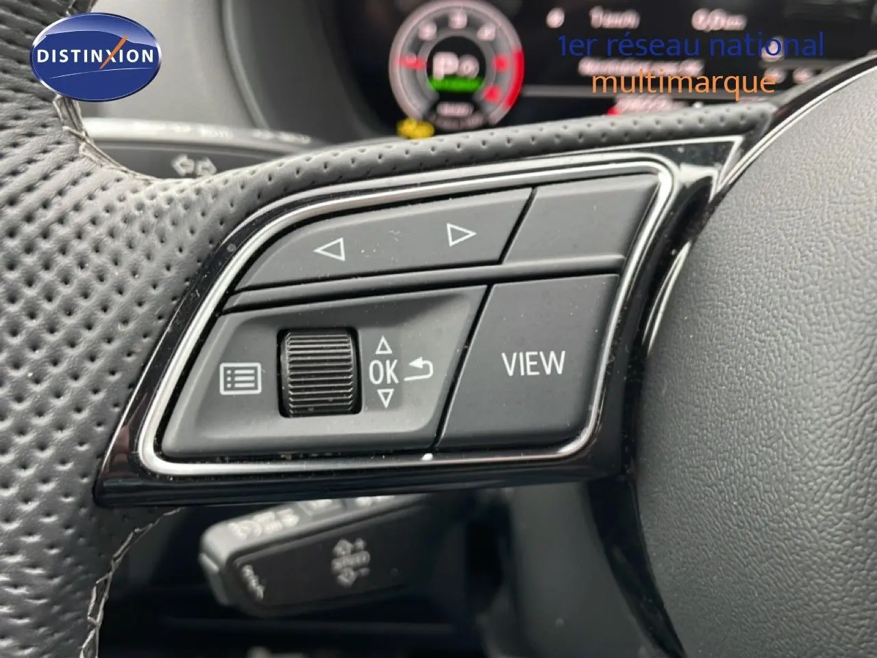 Gros plan sur les commandes gauche du volant en cuir perforé d’un Audi Q2 argent rose, avec affichage numérique en arrière-plan.