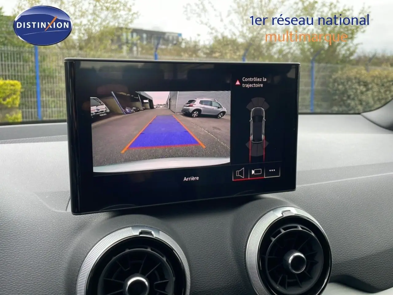 Écran central montrant la caméra de recul d’un Audi Q2 argent rose, avec vue arrière et guidage de trajectoire.