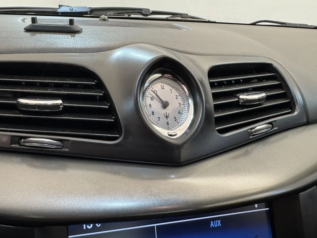 Gros plan sur l'horloge centrale et les aérateurs noirs du tableau de bord gris d'une Maserati Granturismo S 4.7 2010.