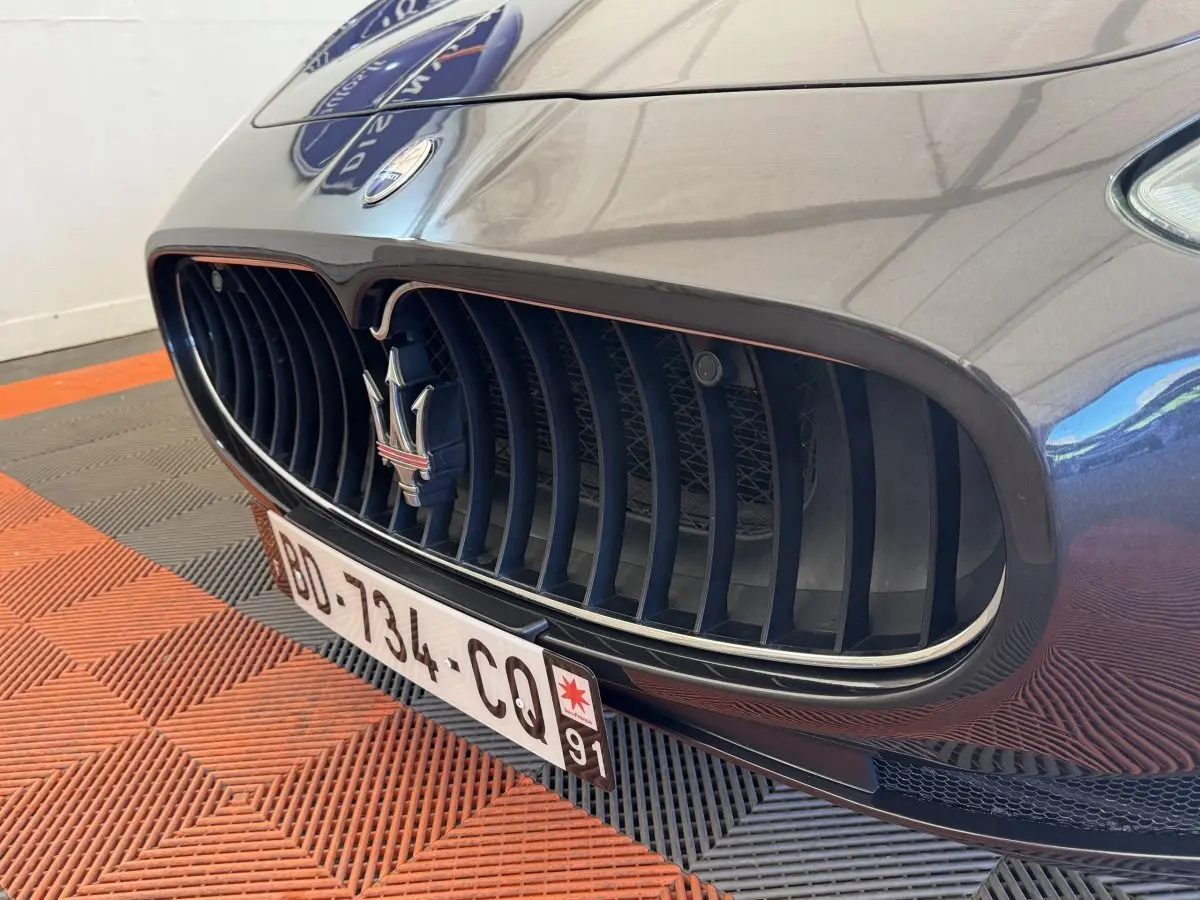 Gros plan sur la calandre avant gris foncé de la Maserati Granturismo S 4.7 avec logo trident et plaque d'immatriculation.