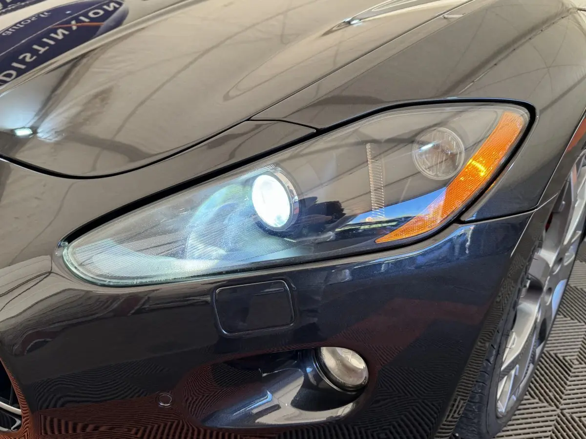 Gros plan sur l'avant droit gris foncé d'une Maserati Granturismo S 4.7 avec phares bi-xénon allumés.