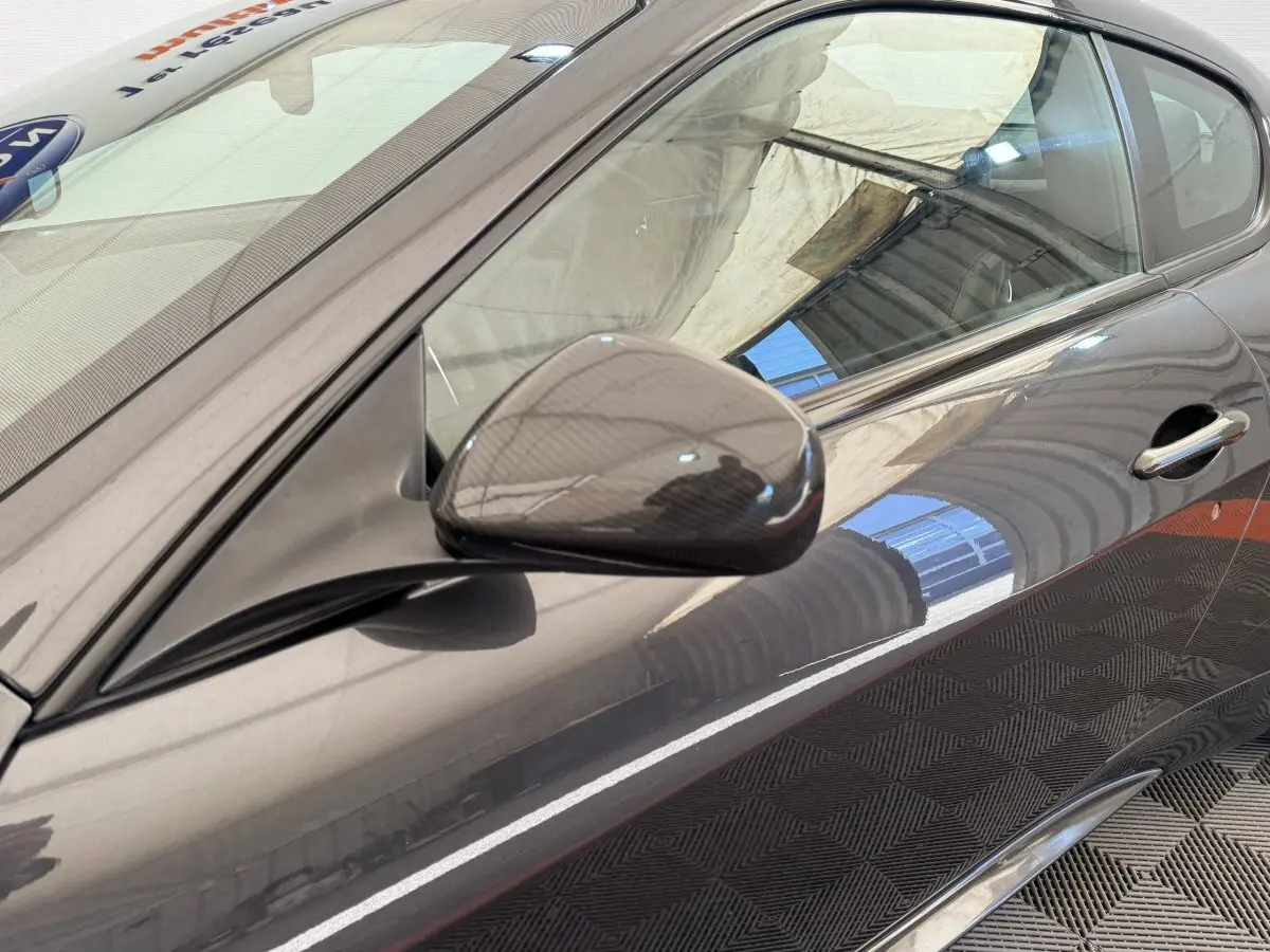 Vue rapprochée du côté gauche d'une Maserati Granturismo S 4.7 gris foncé, mettant en valeur le rétroviseur carbone.
