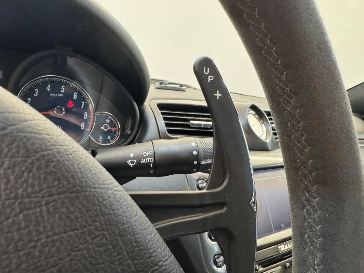 Gros plan sur la palette de changement de vitesse droite en daim du volant d'une Maserati Granturismo S 4.7 gris foncé, tableau de bord visible.