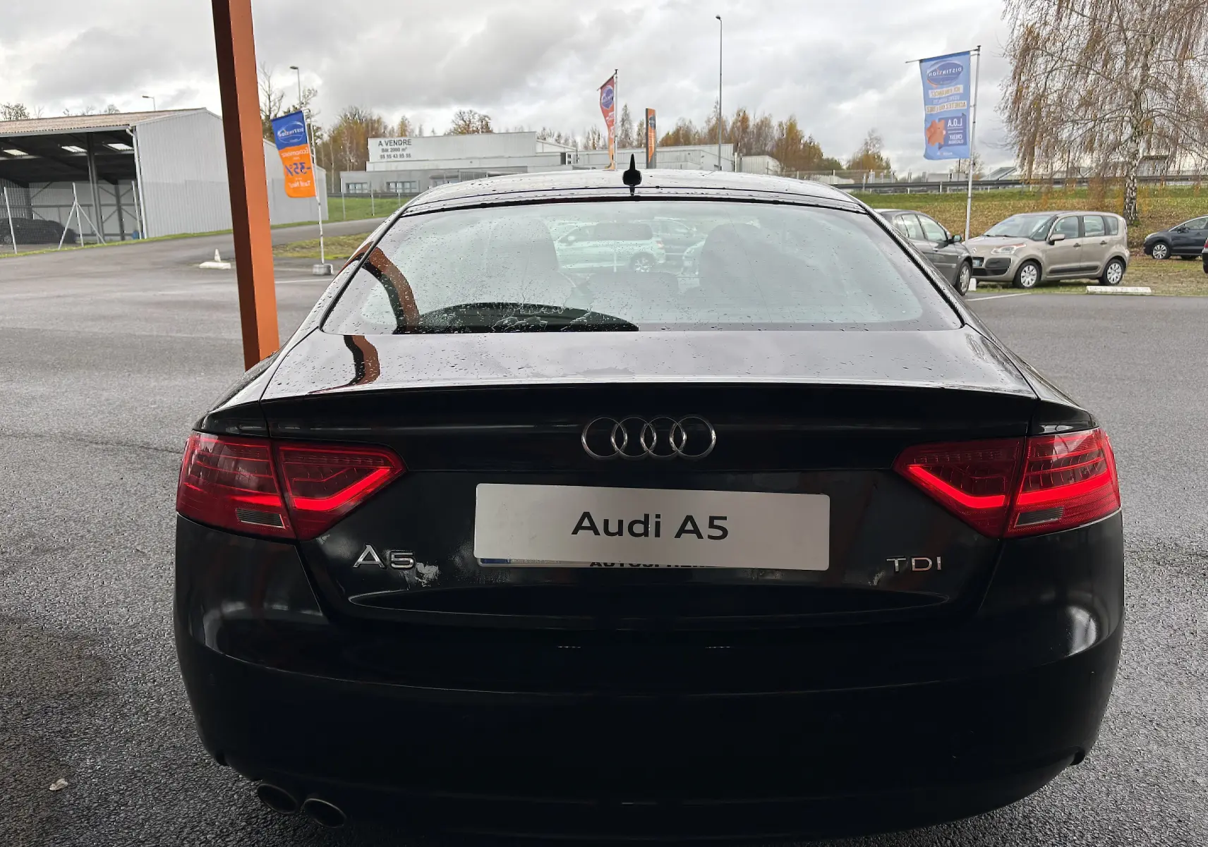 Vue arrière d'une Audi A5 Sportback noire 2013 avec feux allumés et double sortie d'échappement visible.