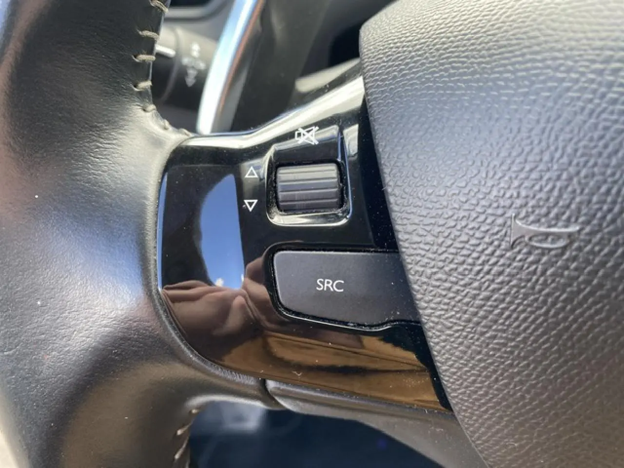 Gros plan sur les commandes audio au volant noir du Peugeot 308 SW gris Hurricane, avec bouton SRC et molette de volume.