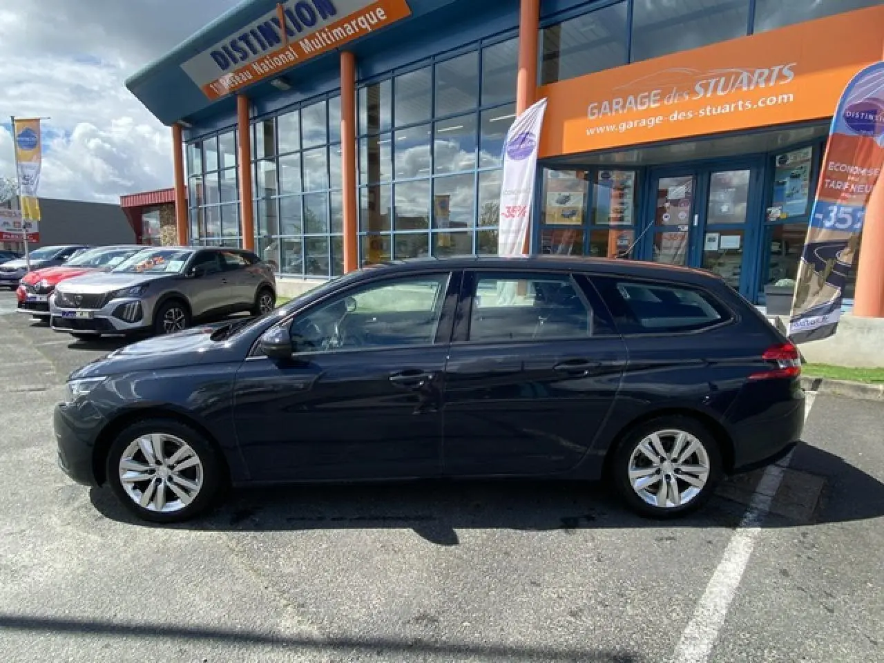 Profil côté gauche d'une Peugeot 308 SW gris hurricane garée devant un garage avec jantes alliage 16 pouces.