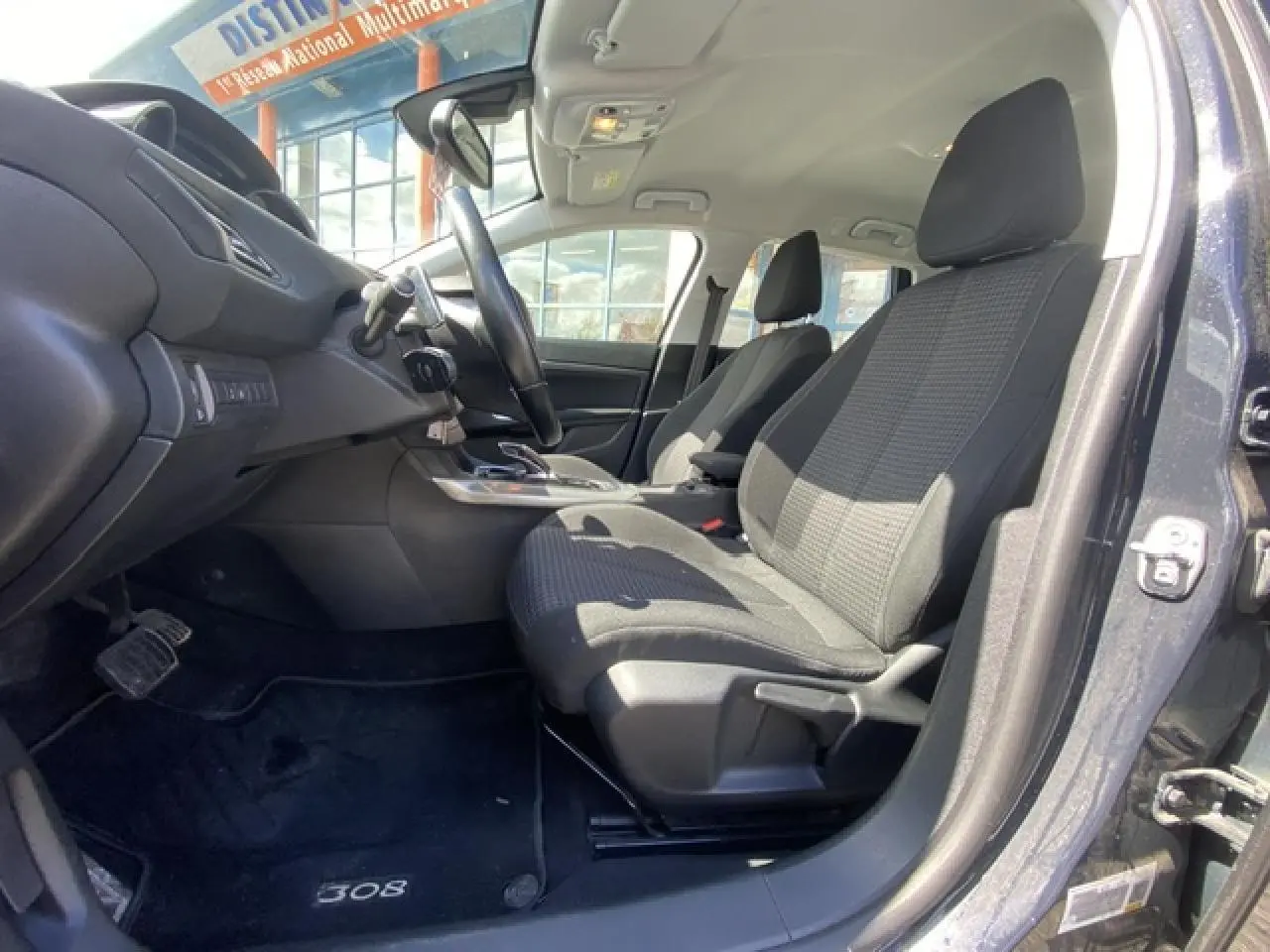 Vue intérieure côté conducteur de la Peugeot 308 SW 2018 gris hurricane, sièges tissu noir et tableau de bord moderne.