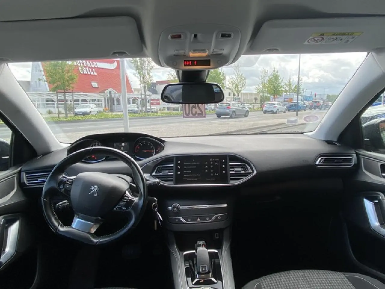 Vue intérieure avant du tableau de bord et volant noir de la Peugeot 308 SW gris Hurricane avec écran tactile central.
