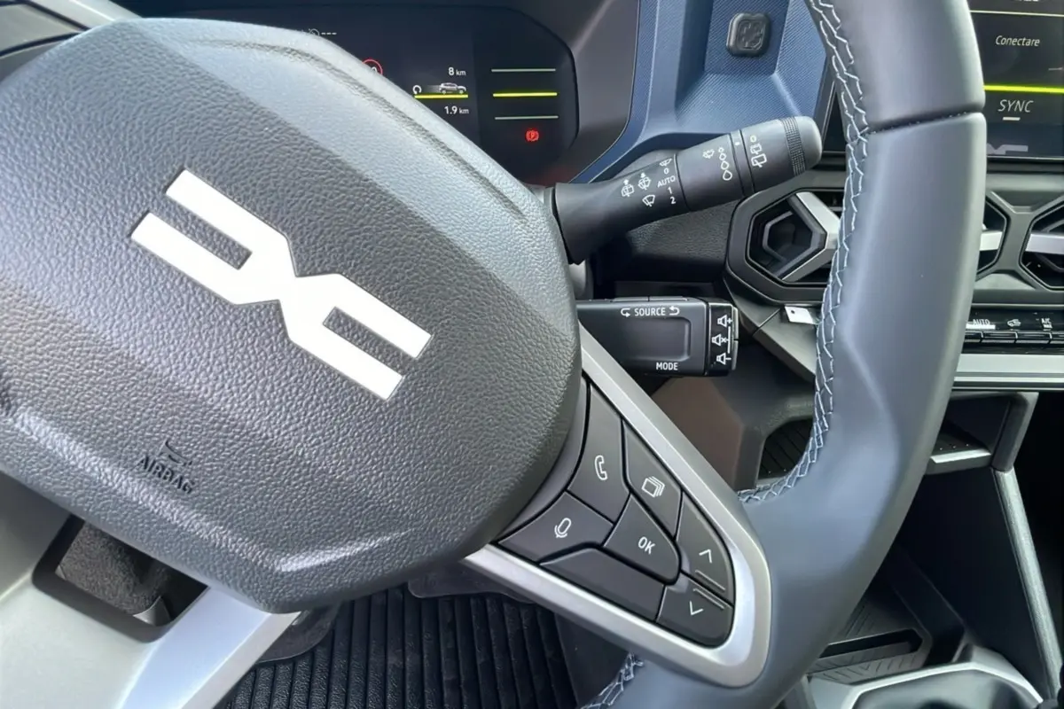 Gros plan sur le volant noir avec commandes intégrées du Dacia Bigster 2025, tableau de bord numérique en arrière-plan.
