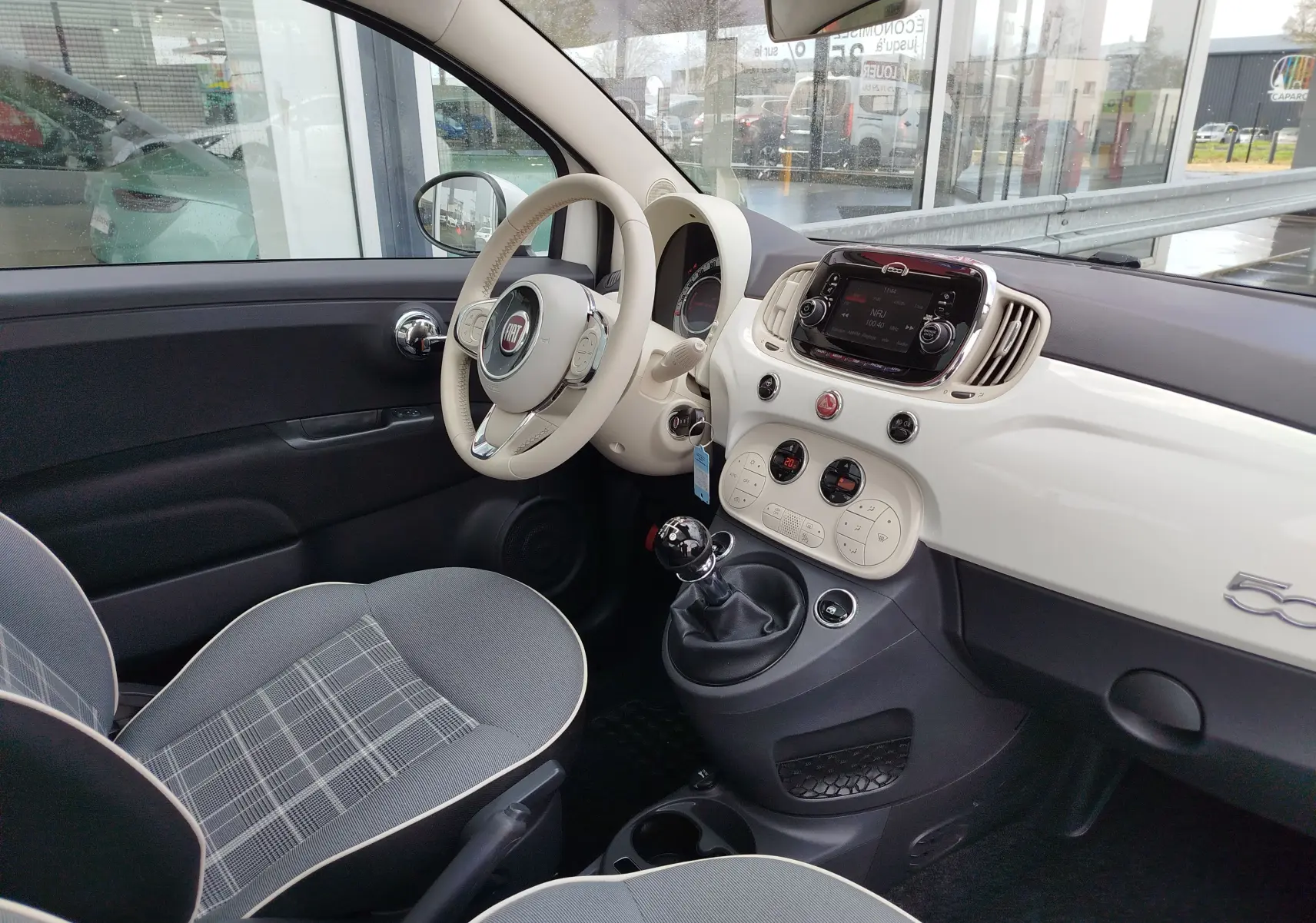 Vue intérieure côté conducteur de la Fiat 500 Lounge blanche, avec tableau de bord crème et volant assorti.