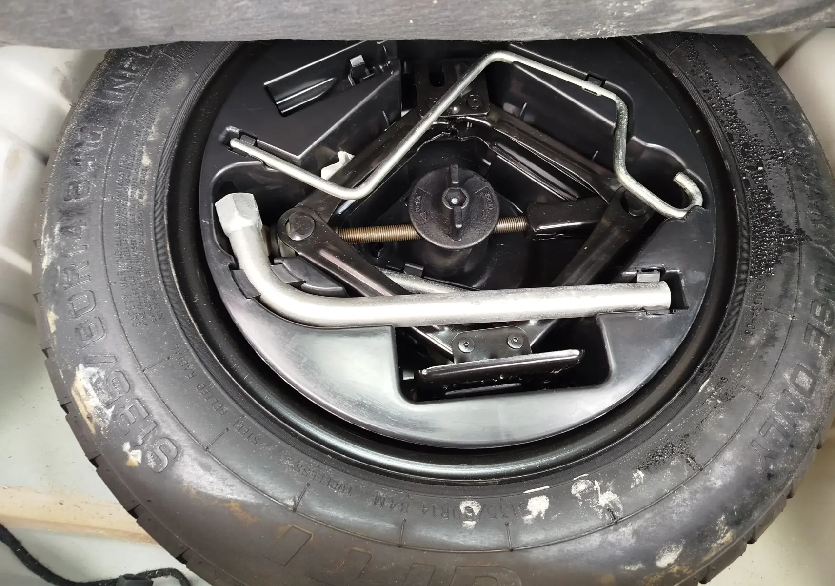 Gros plan sur la roue de secours et les outils de bord du coffre d’une Fiat 500 blanche, version Lounge 2017.