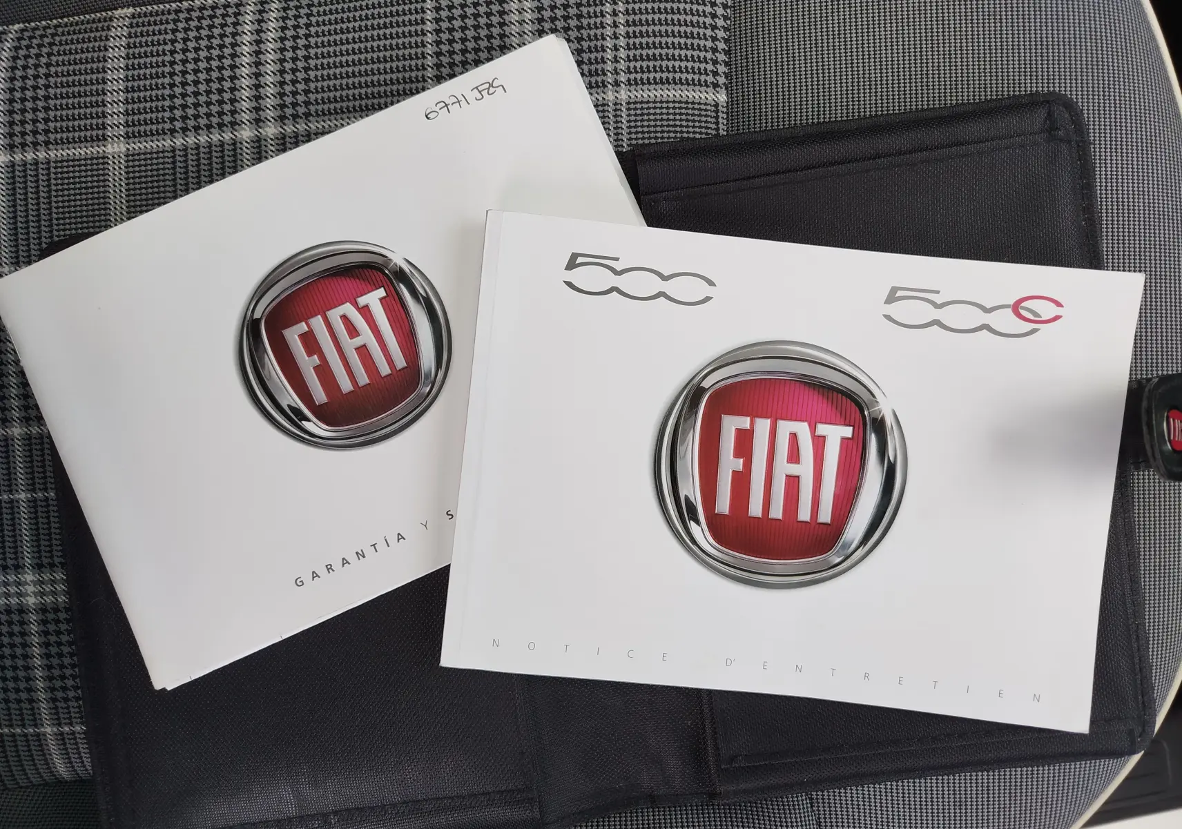 Manuels d'entretien Fiat 500 posés sur un siège à motif pied-de-poule, sans vue du véhicule.