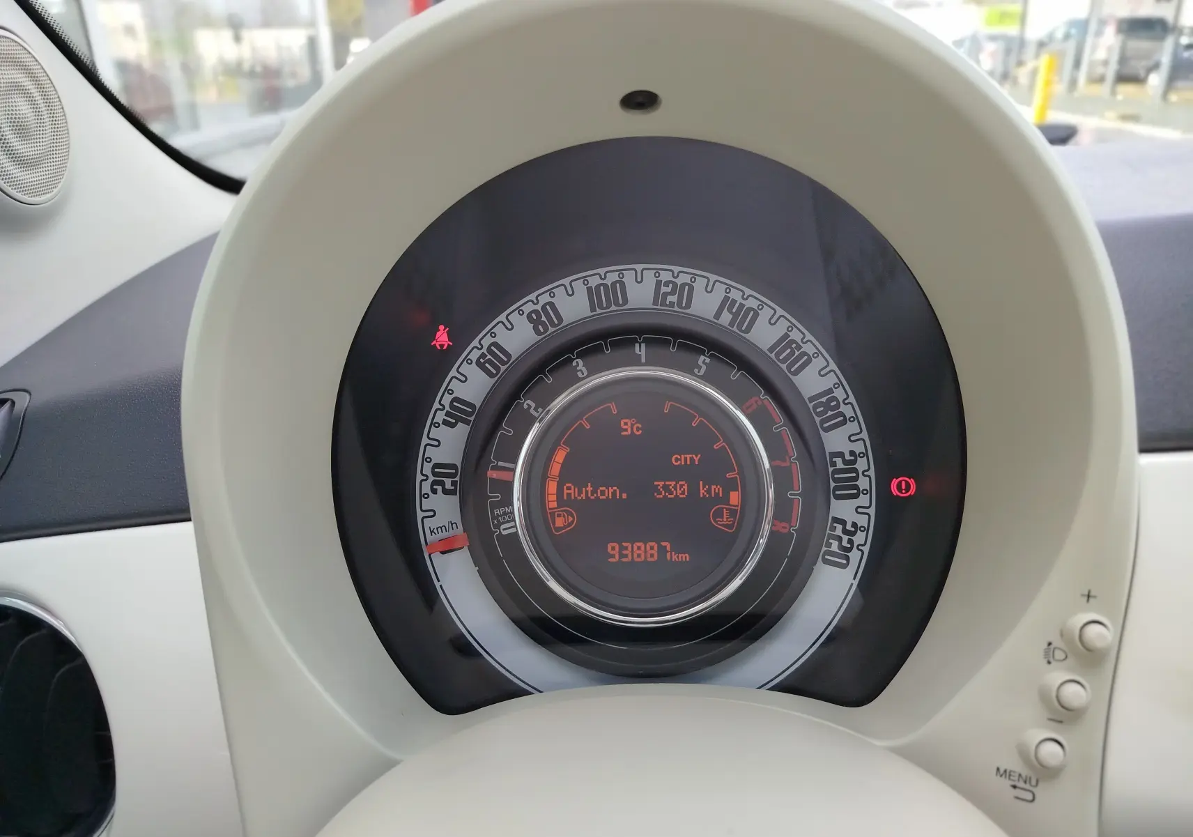 Gros plan sur le compteur central rond de la Fiat 500 blanche, affichant la vitesse et l'autonomie restante.