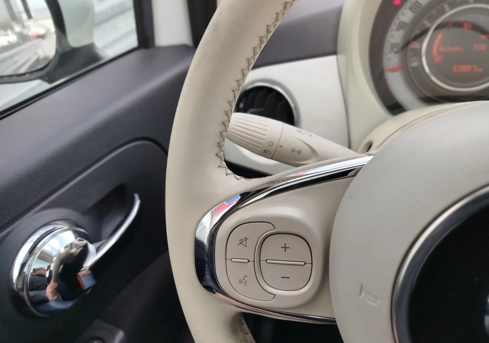 Gros plan sur le volant beige et la commande audio d’une FIAT 500 Bossa Nova White Pastel, tableau de bord partiellement visible.