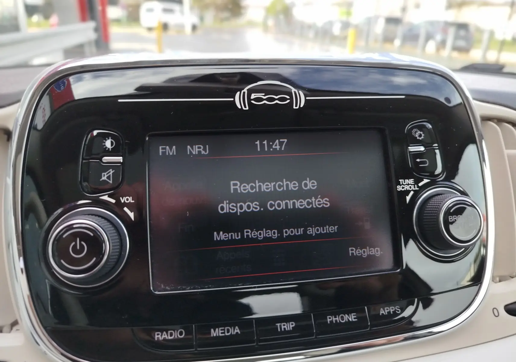 Gros plan sur l’écran tactile noir brillant du tableau de bord de la Fiat 500 blanche, affichant la recherche de dispositifs connectés.