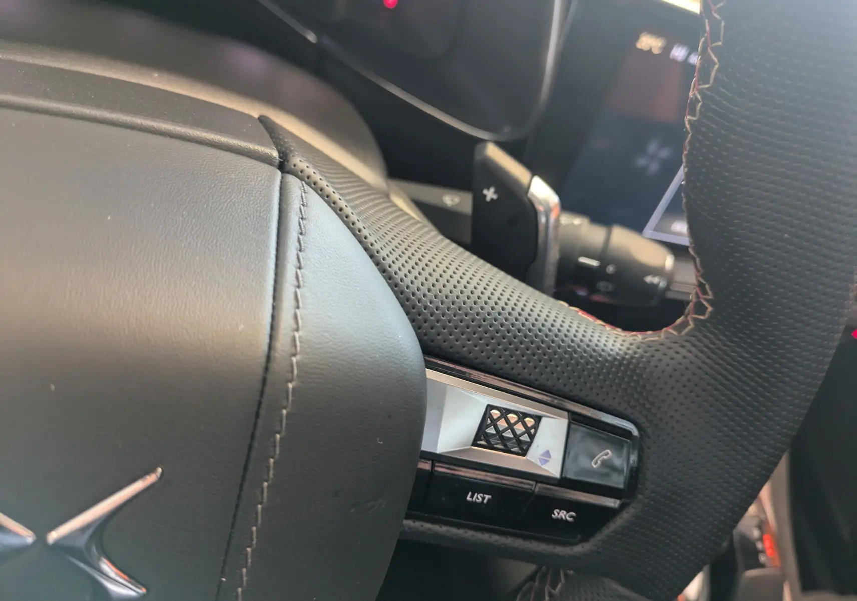 Gros plan sur le volant en cuir perforé noir du DS7 2025, avec commandes intégrées et surpiqûres apparentes.