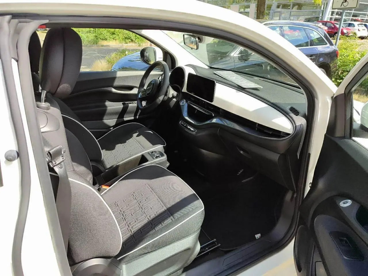 Vue 3/4 avant droite d'une FIAT 500 électrique blanche avec calandre épurée et jantes multibranches.