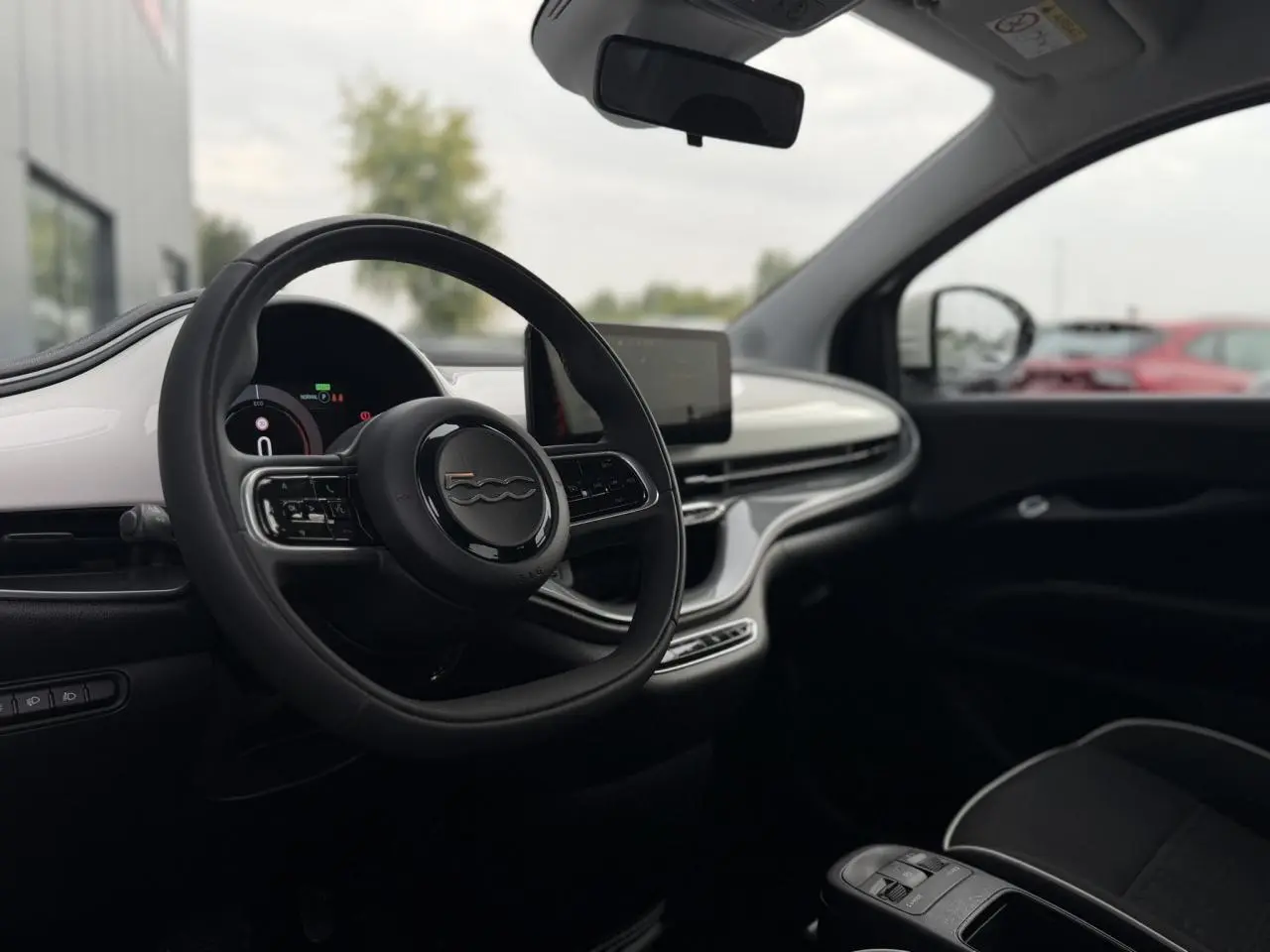 Intérieur de la Fiat 500 électrique 2024 vu côté conducteur, volant noir et tableau de bord blanc brillant.