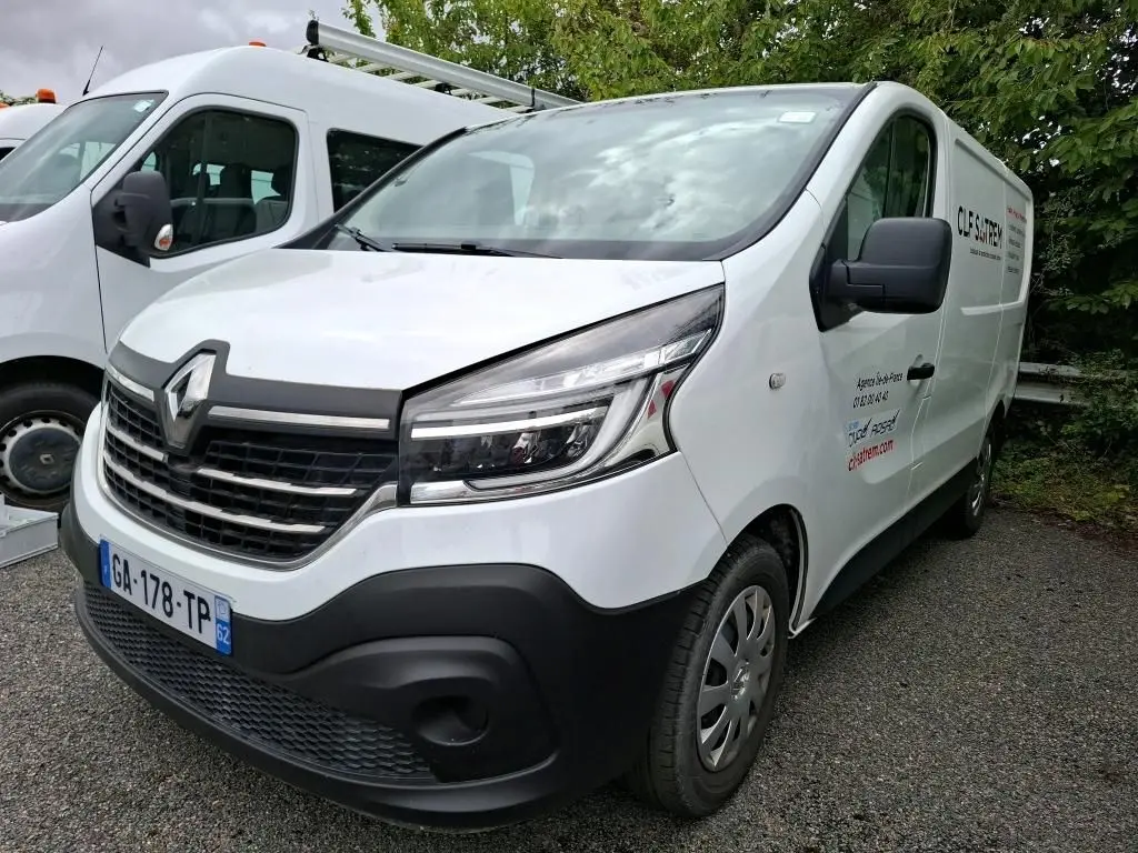 Renault Trafic Fourgon blanc vu en 3/4 avant droit avec marquage commercial sur la porte latérale droite.