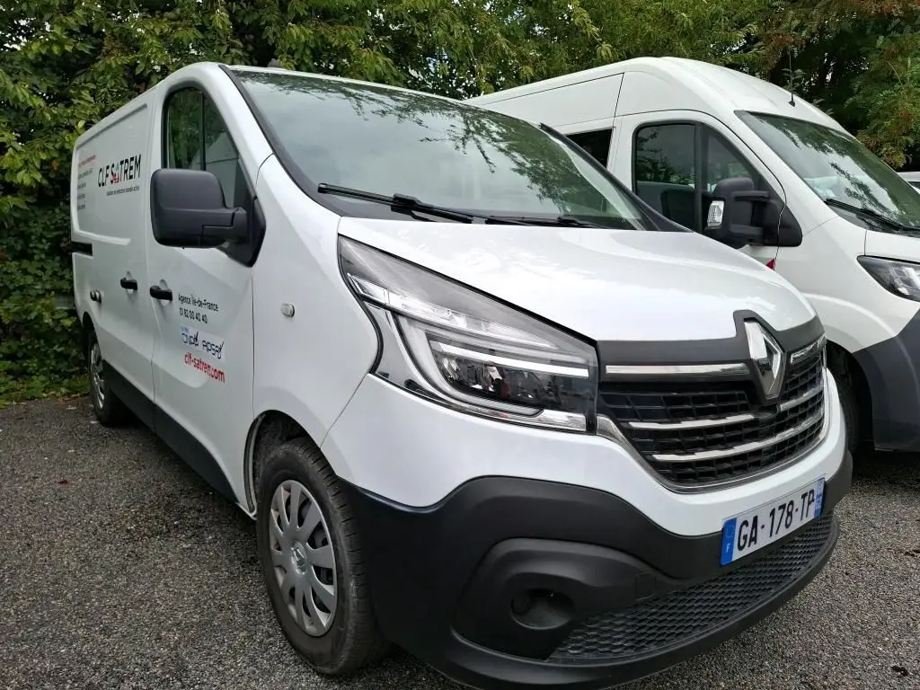 Renault Trafic Fourgon blanc vu en 3/4 avant droit, avec logo et marquage commercial sur la porte côté gauche.