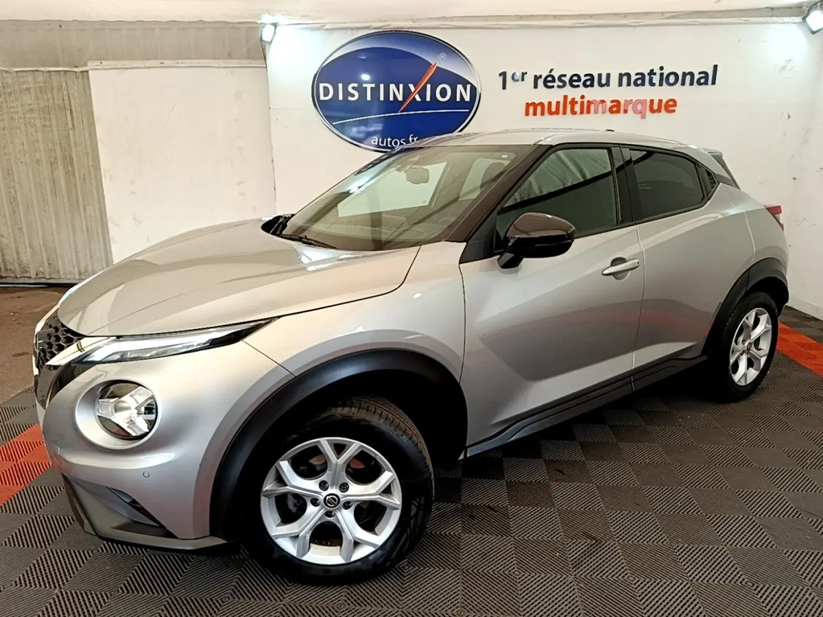 Nissan Juke gris clair en 3/4 avant droit, avec rétroviseurs ton caisse et jantes alliage visibles.