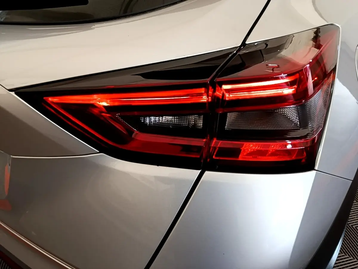 Gros plan sur le feu arrière droit rouge et noir d’un Nissan Juke gris clair, version 2022, avec carrosserie lisse.