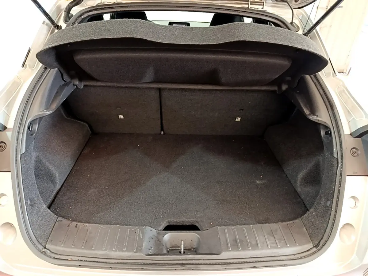 Coffre ouvert vu de l'arrière d'un Nissan Juke gris clair, montrant l'espace de chargement vide et la tablette de coffre relevée.