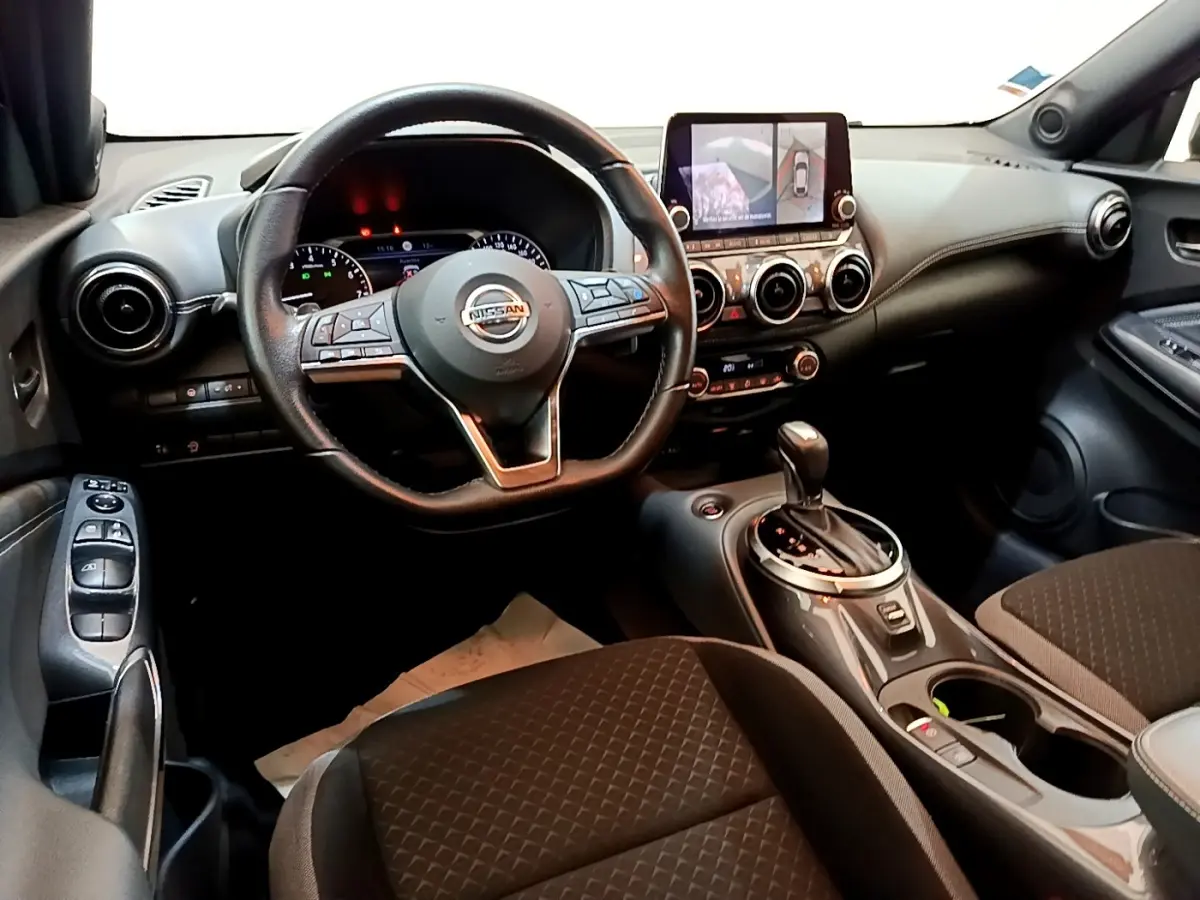 Vue intérieure avant du Nissan Juke 2022 avec volant cuir, écran tactile central et levier de boîte automatique.
