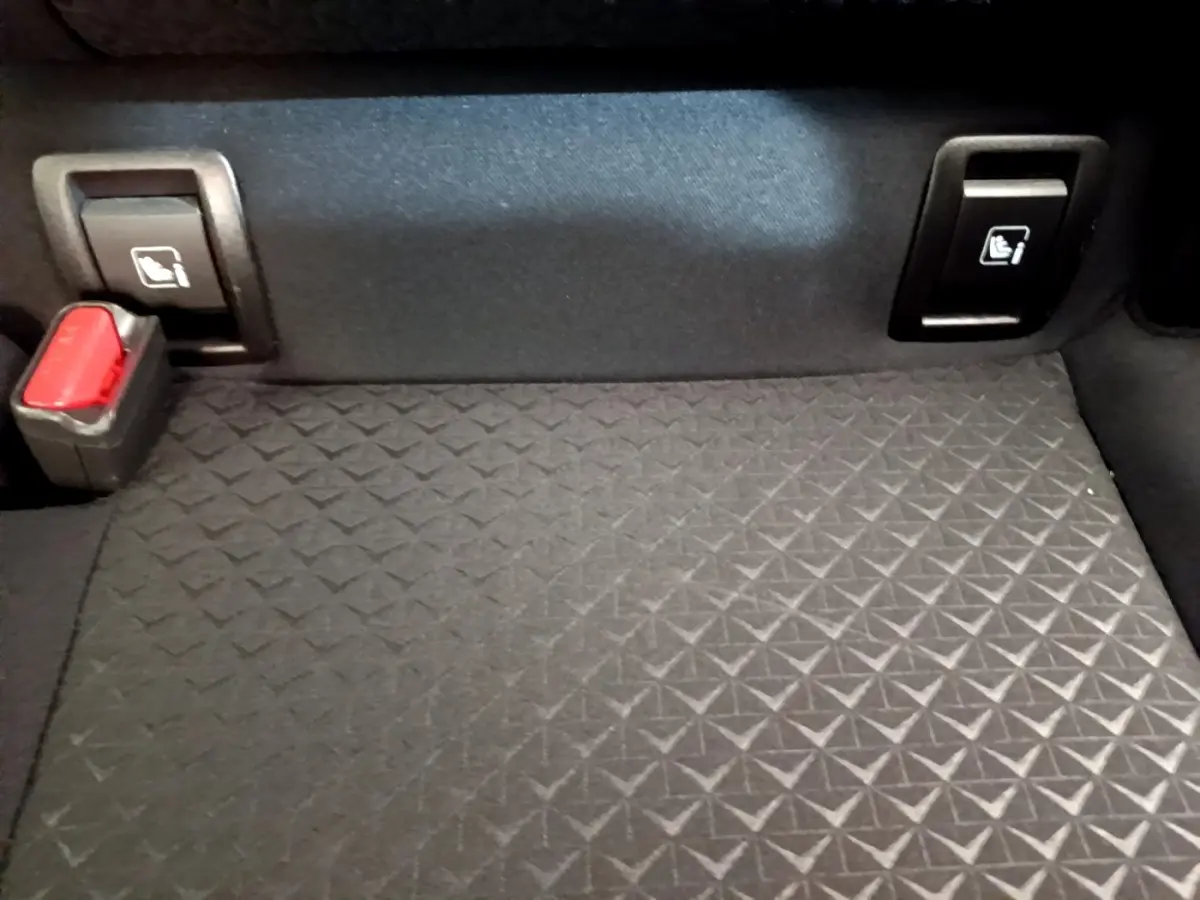 Détail du coffre noir du Nissan Juke 2022 avec boutons de rabattement des sièges arrière et boucle de ceinture rouge.