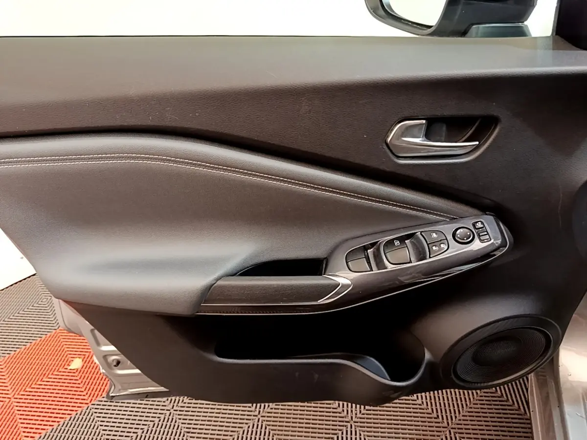 Vue rapprochée de la porte avant gauche du Nissan Juke gris clair 2022, avec commandes électriques et poignée intégrée.