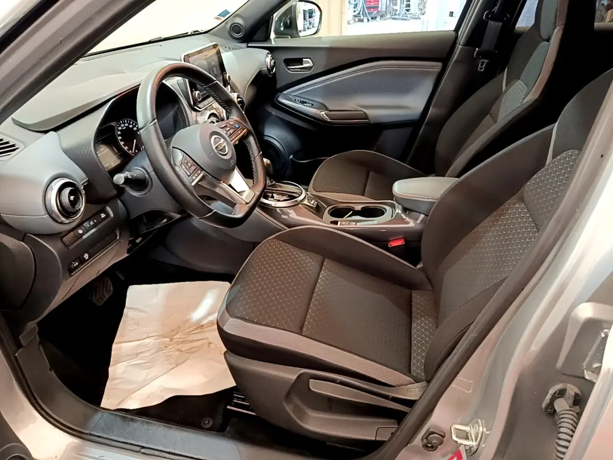 Vue intérieure côté conducteur du Nissan Juke gris clair 2022, montrant sièges et tableau de bord avec écran tactile.