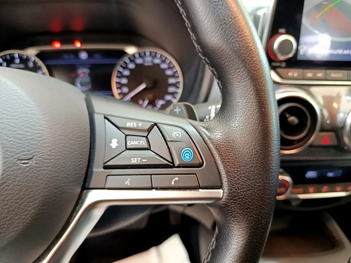 Gros plan sur le volant en cuir noir du Nissan Juke 2022 avec commandes multifonctions et tableau de bord flou en arrière-plan.