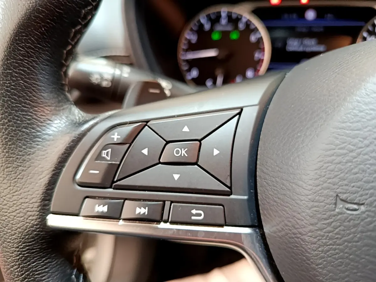 Gros plan sur les commandes au volant en cuir noir du Nissan Juke gris clair, avec tableau de bord flou en arrière-plan.